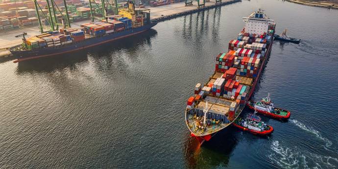 Container ship being pushed into dock by two tug boats